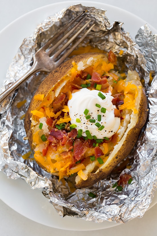 Baked potato made in the slow cooker. Its cut open and topped with cheddar, bacon, sour cream and chives. Overhead image.