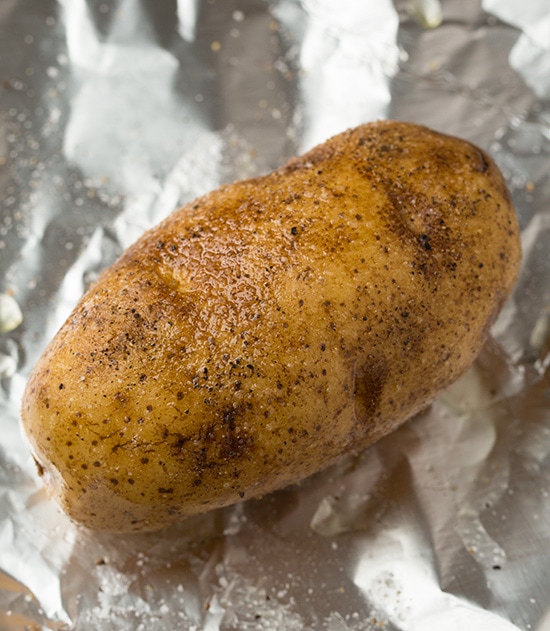 Brushing potatoes with oil and seasoning with salt and pepper.