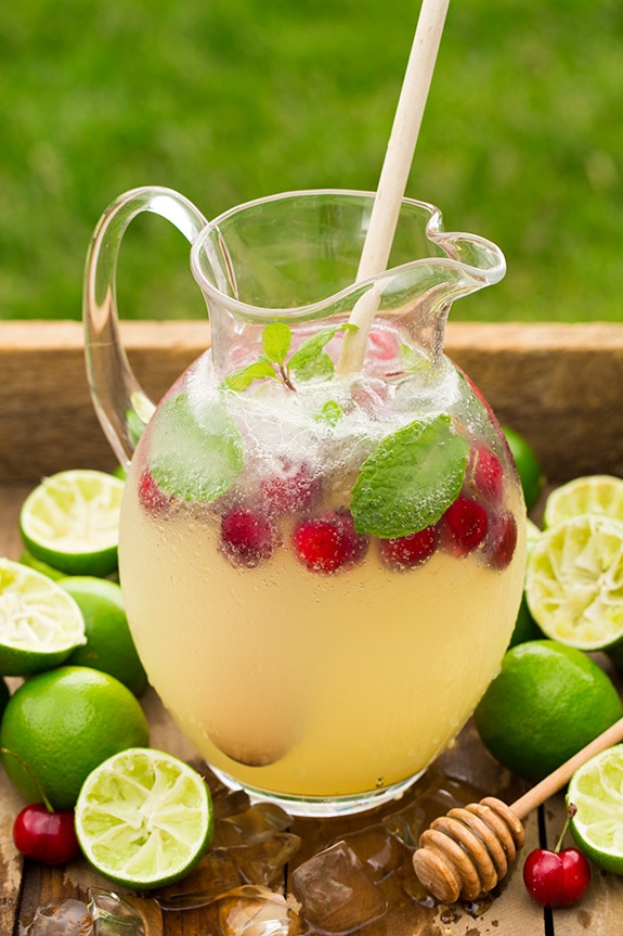 limeade in glass pitcher with raspberries and mint leaves, on tray with limes