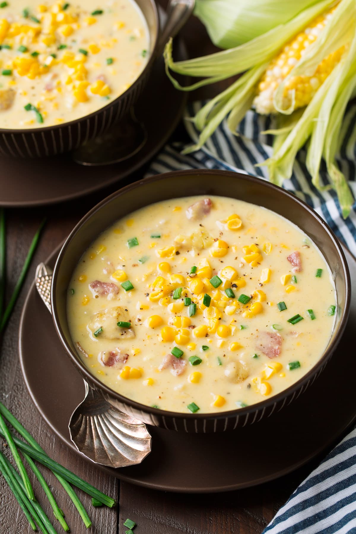 Corn Chowder in two serving bowls. Chowder has fresh pieces of corn, chunks of ham and is garnished with chives.