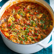 Cabbage Roll Soup shown in a large white pot on a blue cloth.