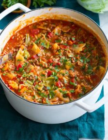 Cabbage Roll Soup shown in a large white pot on a blue cloth.