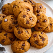 Image of pumpkin chocolate chip cookies stacked on a white serving plate.