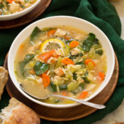 Lemon Chicken Orzo Soup in a white serving bowl on a wooden plate.