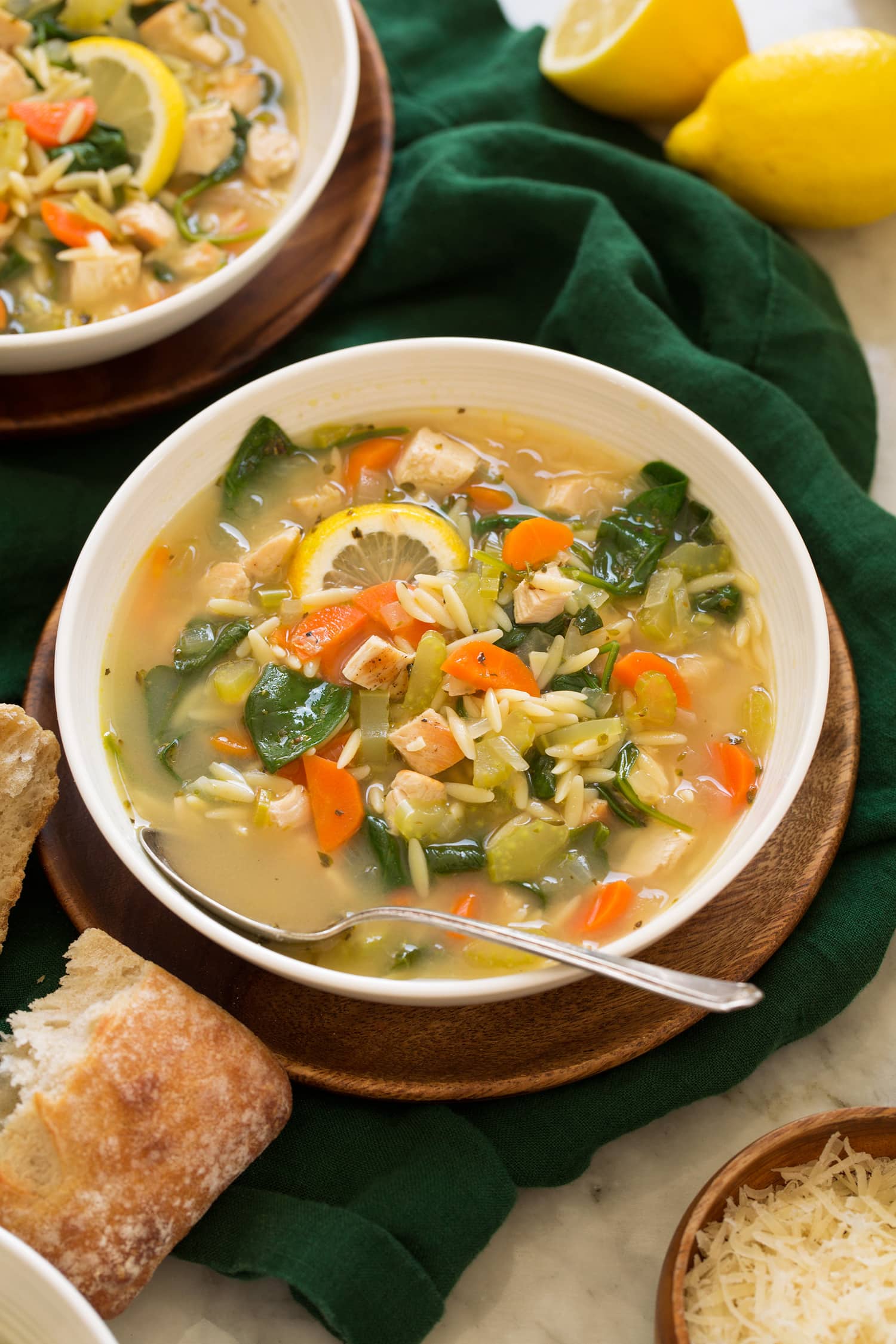 Lemon Chicken Orzo Soup in a white serving bowl on a wooden plate.