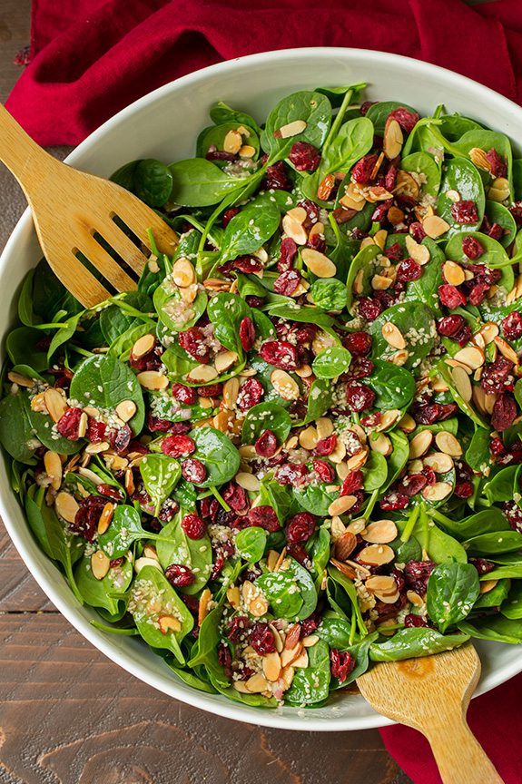 Overhead image of spinach salad in a large salad bowl with wooden serving spoons.