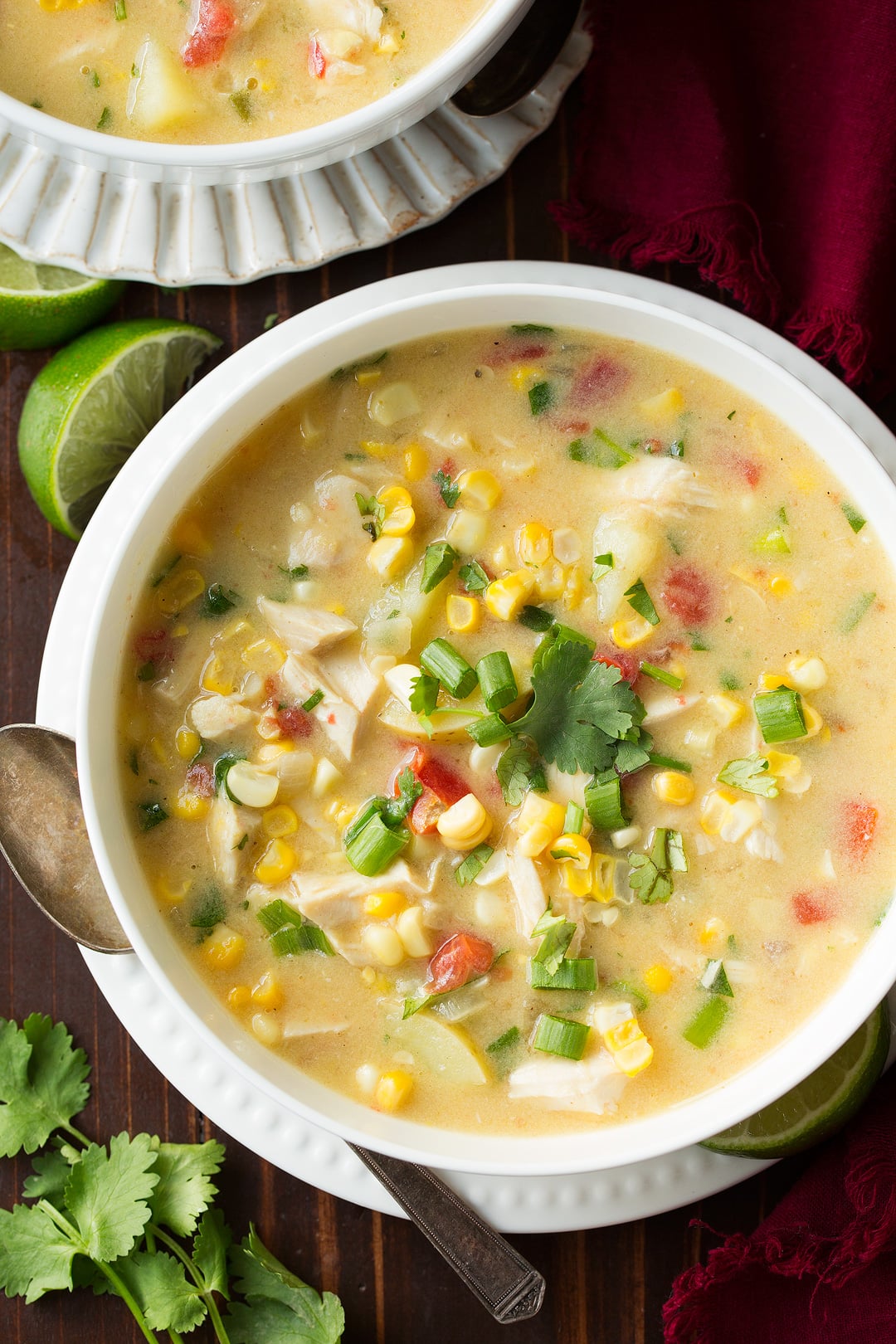 Coconut Chicken Corn Chowder in a white bowl sitting on a white plate over a dark wooden surface.