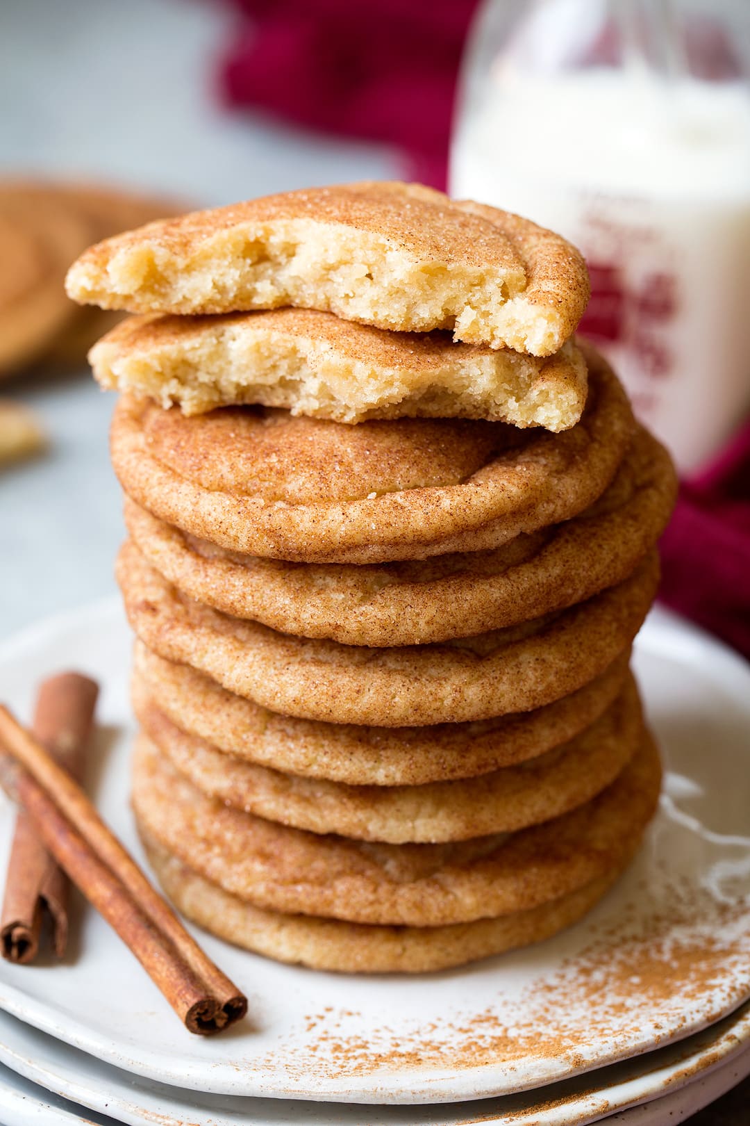 Stack of snickerdoodle cookies on a plate with one cooke on top broken in half to show texture of interior.