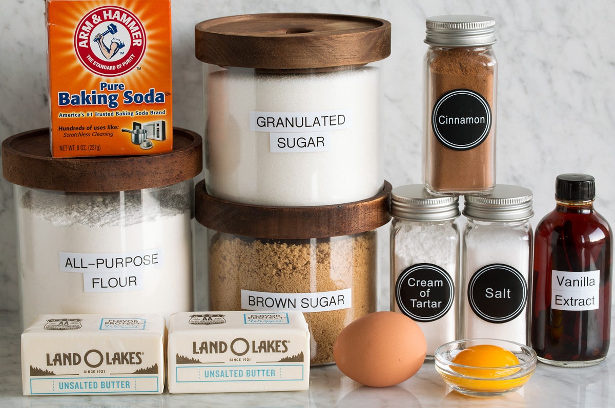 Image of ingredients used to make Snickerdoodle cookies. Includes flour, granulated sugar, brown sugar, egg, egg yolk, butter, salt, cream of tartar, cinnamon, vanilla and baking soda.