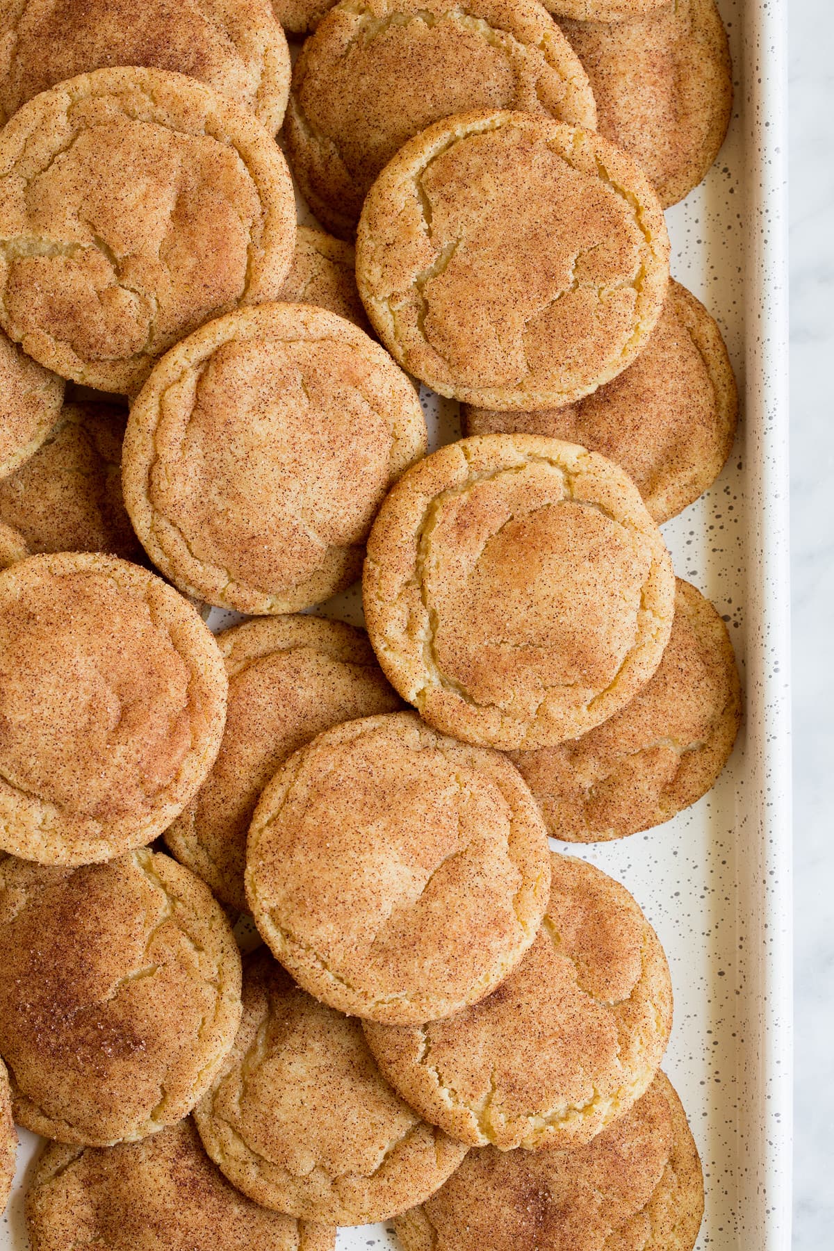 Overhead image of a white cookie sheet layered with snickerdoodle cookies.