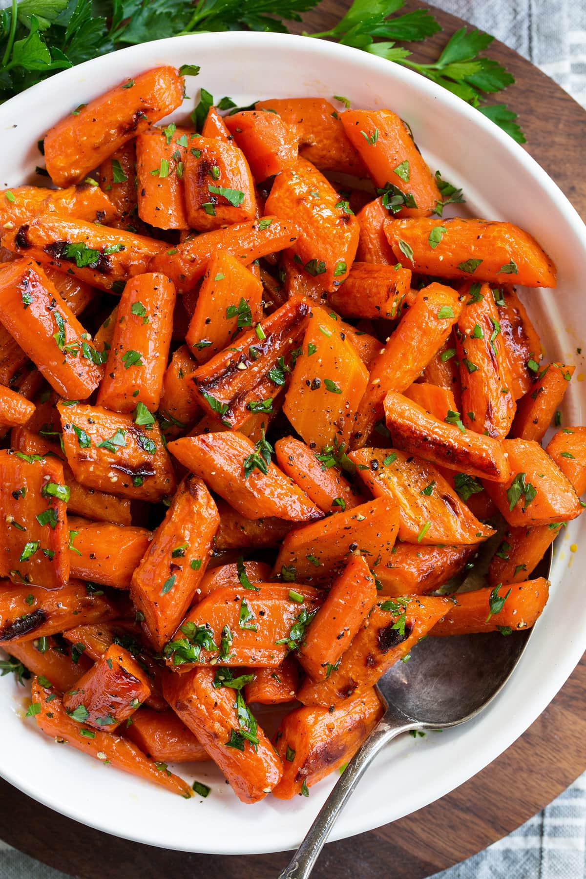 Photo: Overhead angle of roasted carrots in a serving bowl set over a wooden platter.