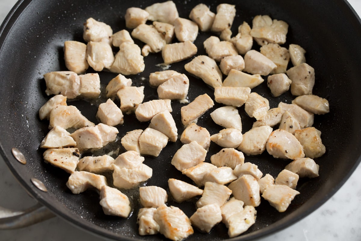 Showing how to make chicken fried rice. Sautéing small chicken breast pieces in a skillet until cooked through.