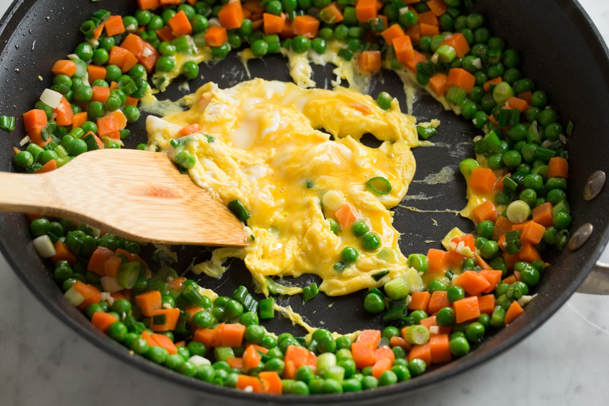 Scrambling eggs in the center of a ring of vegetables in a skillet for chicken fried rice.