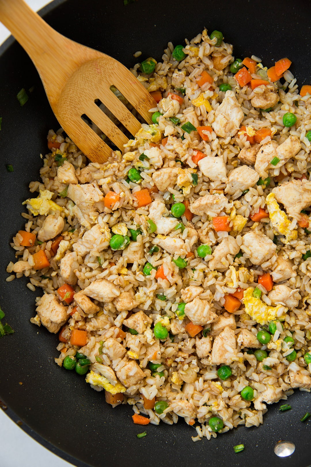 Chicken fried rice in a wok with a wooden spatula. 