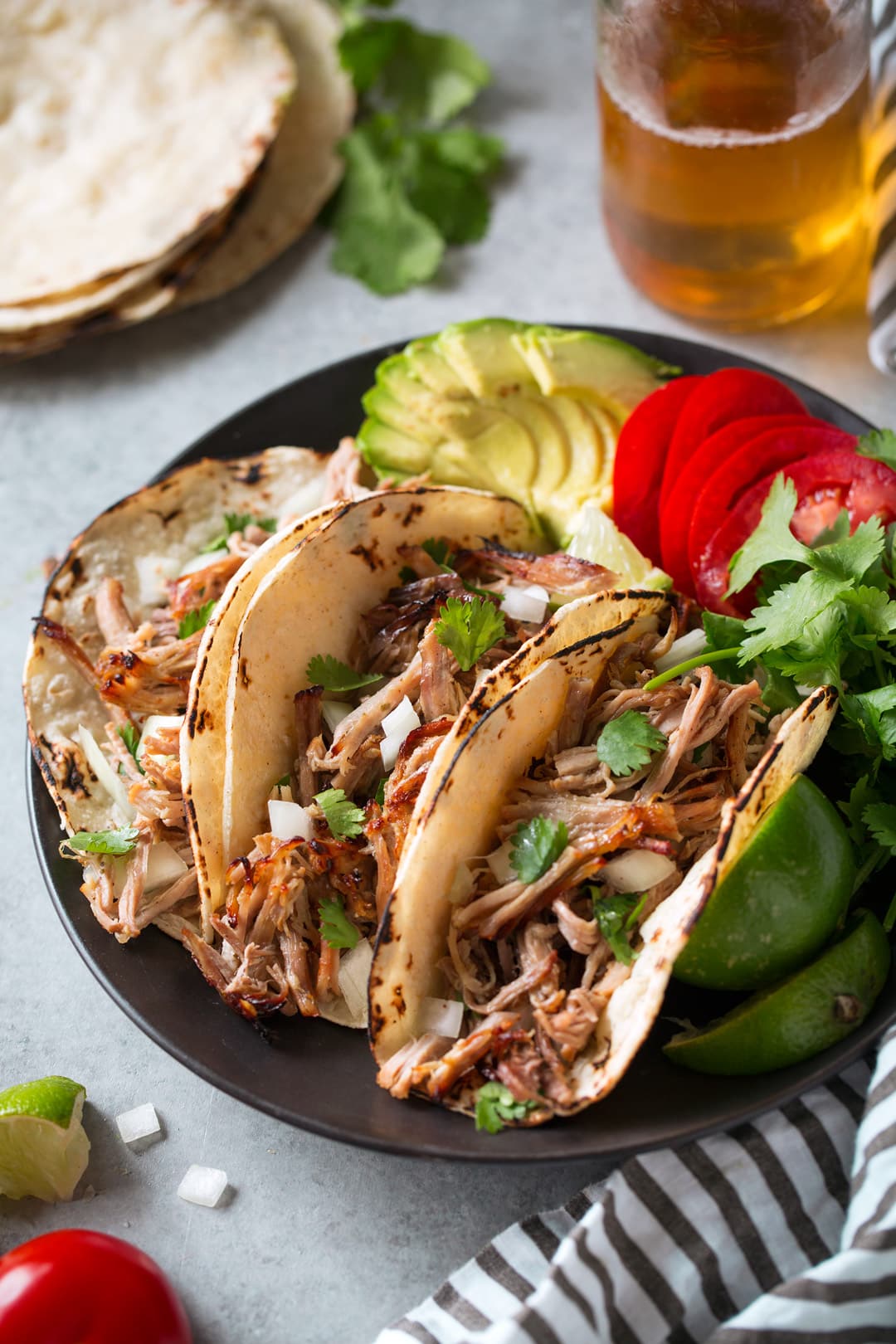 Three carnitas tacos shown here on black a plate in corn tortillas