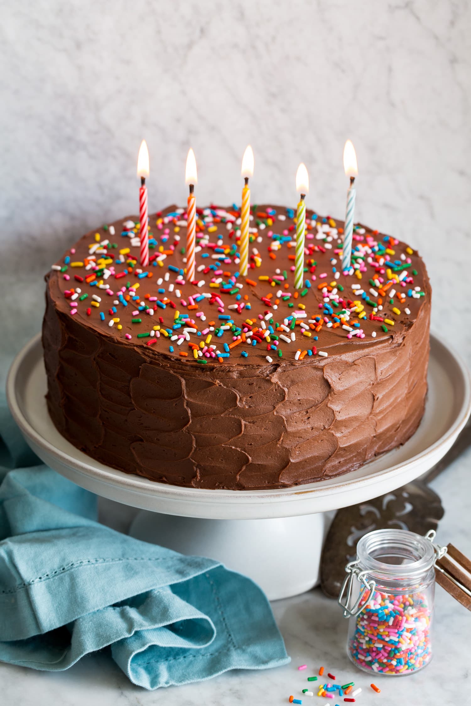 Whole cake with chocolate buttercream frosting and lit candles.