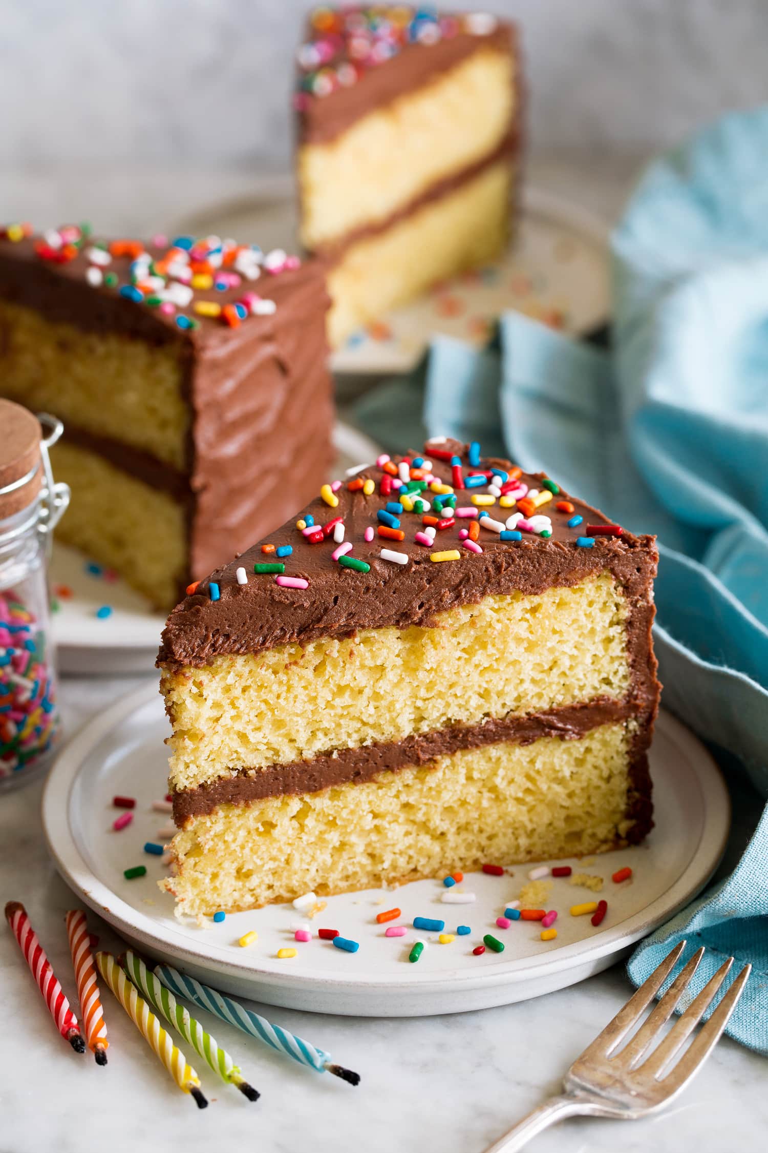 Slice of homemade yellow cake with chocolate frosting and sprinkles.