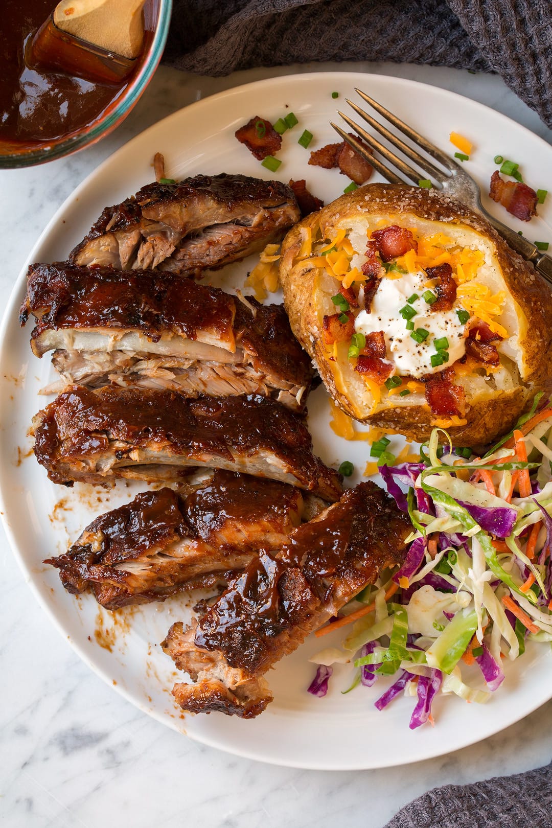 Crockpot ribs on white plat with baked potato and coleslaw