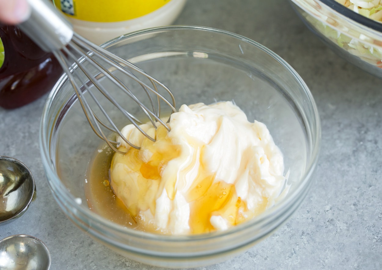 Making coleslaw dressing in mixing bowl with 3 ingredients including mayonnaise, honey, apple cider vinegar.