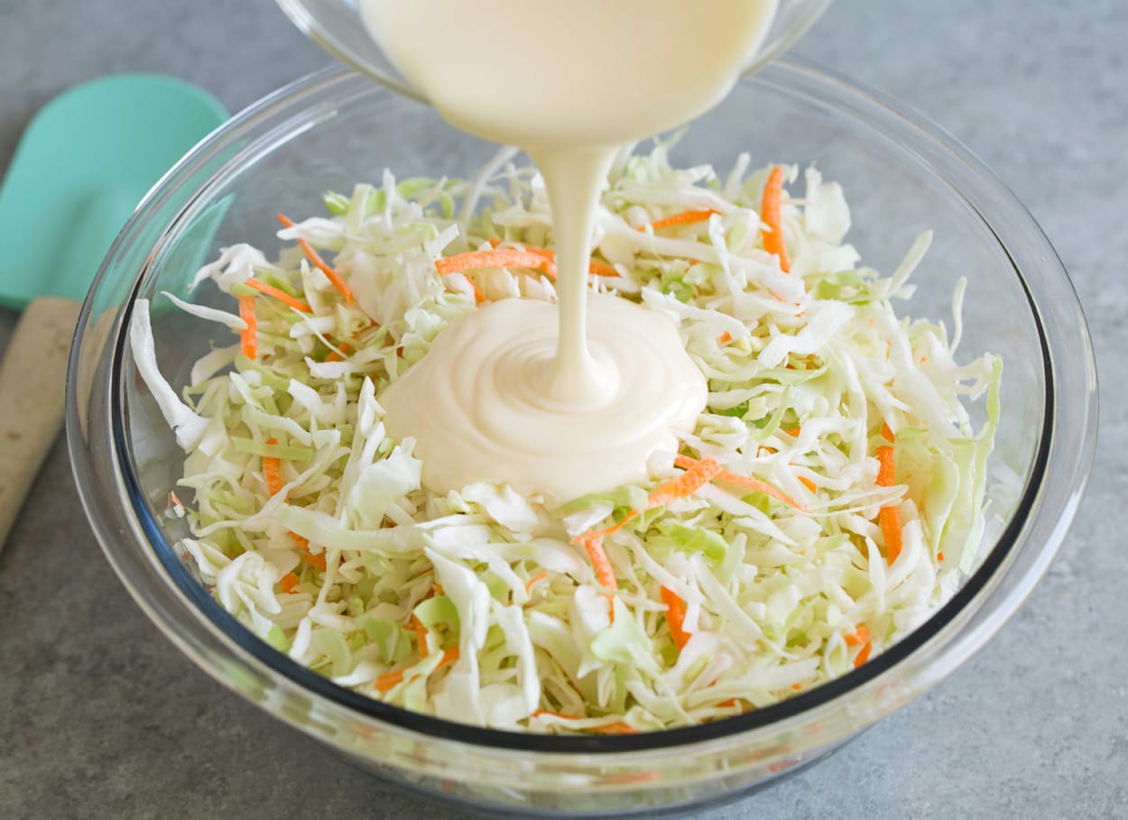 Adding coleslaw dressing to coleslaw in mixing bowl.