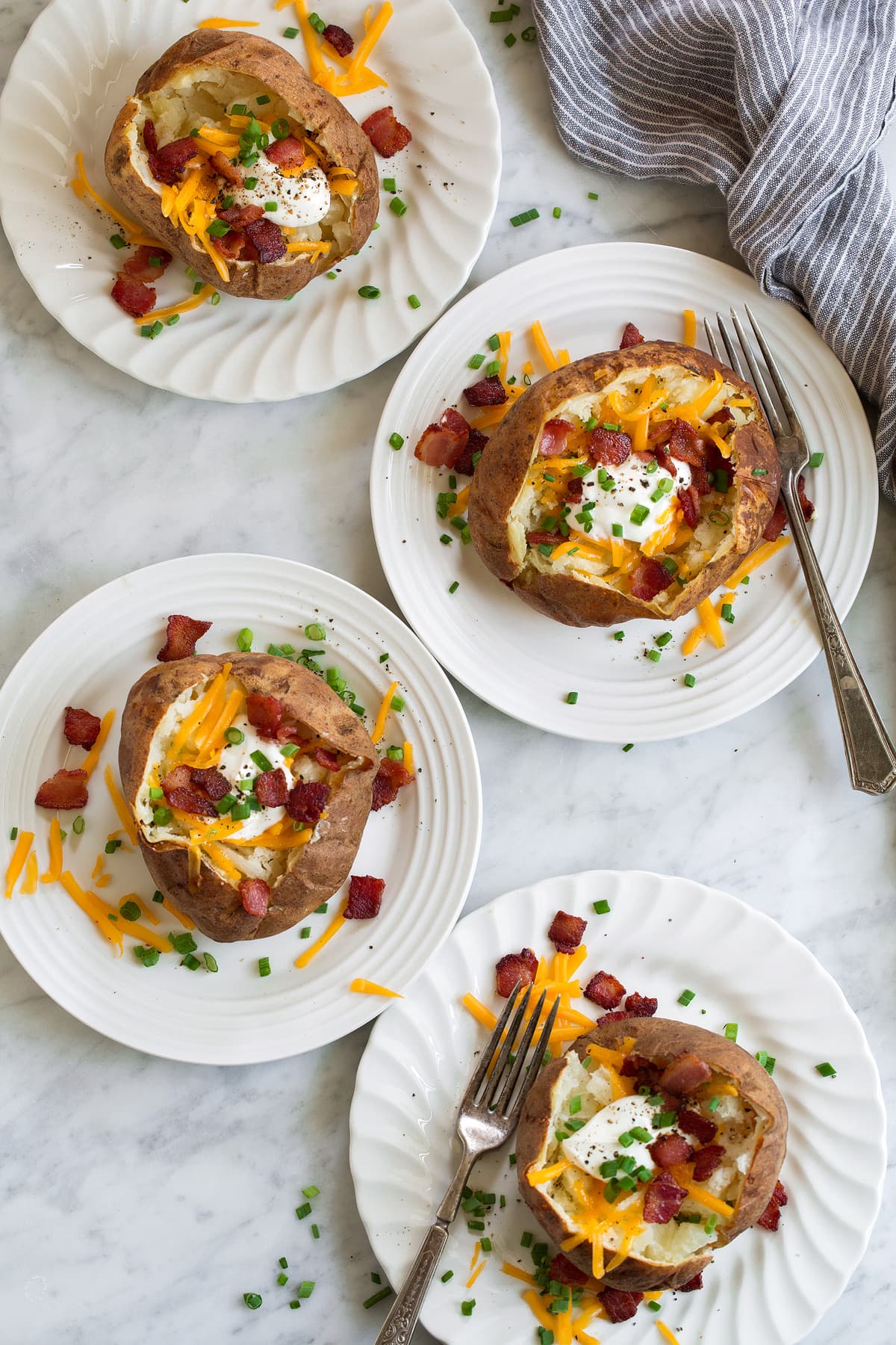 four perfect Baked Potatoes on white plates