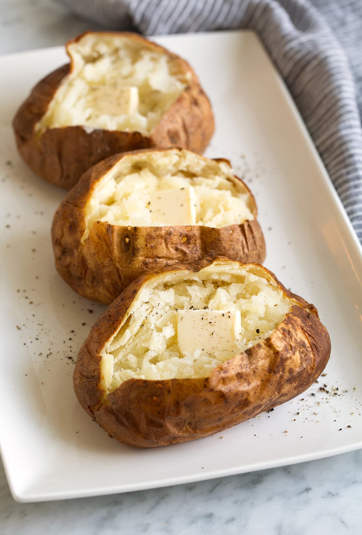 three baked potatoes topped with butter on white plate