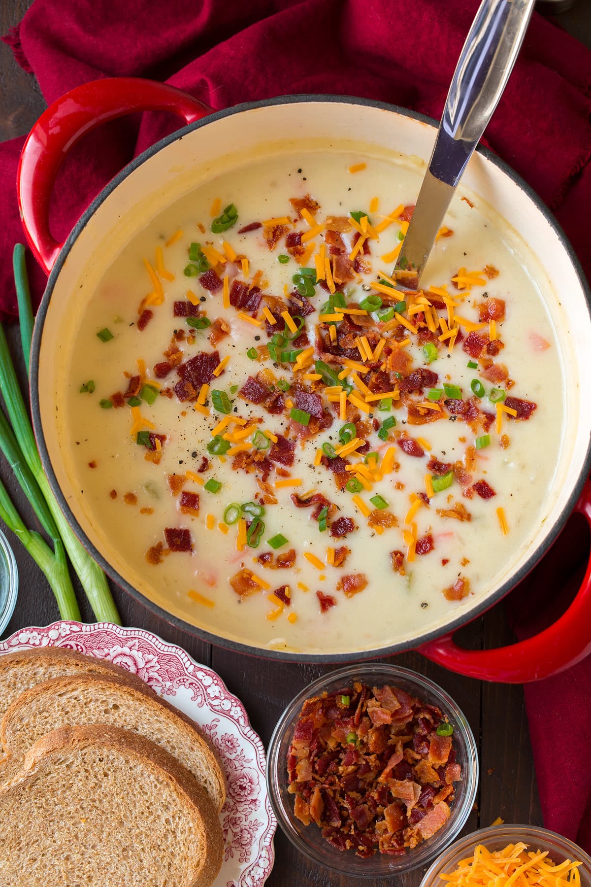 Overhead photo of potato soup in a large red and white pot set over a wooden tabletop with serving suggestions to the side.