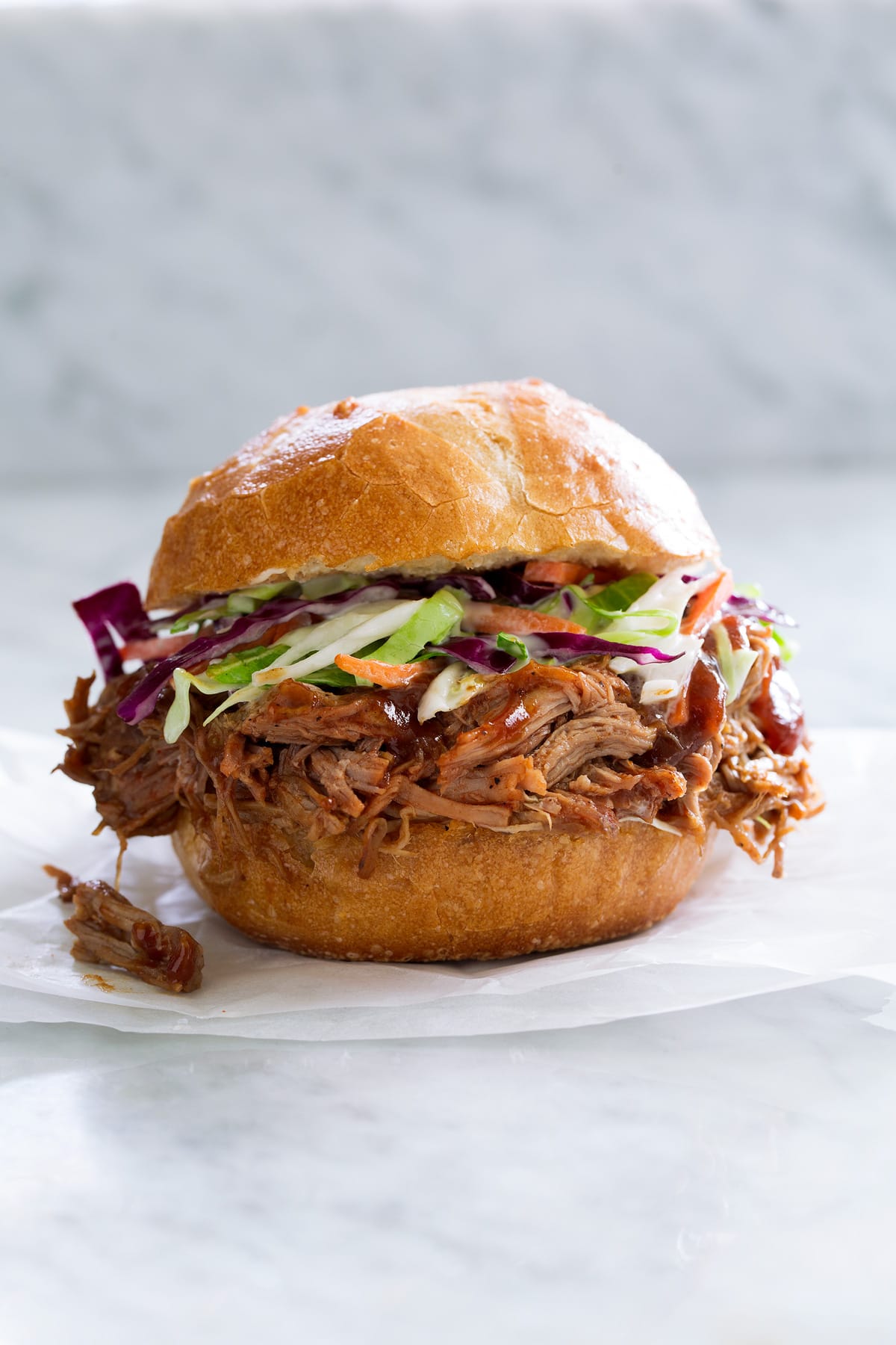 Pulled Pork shown here in a bun with coleslaw sitting on parchment paper on a marble surface