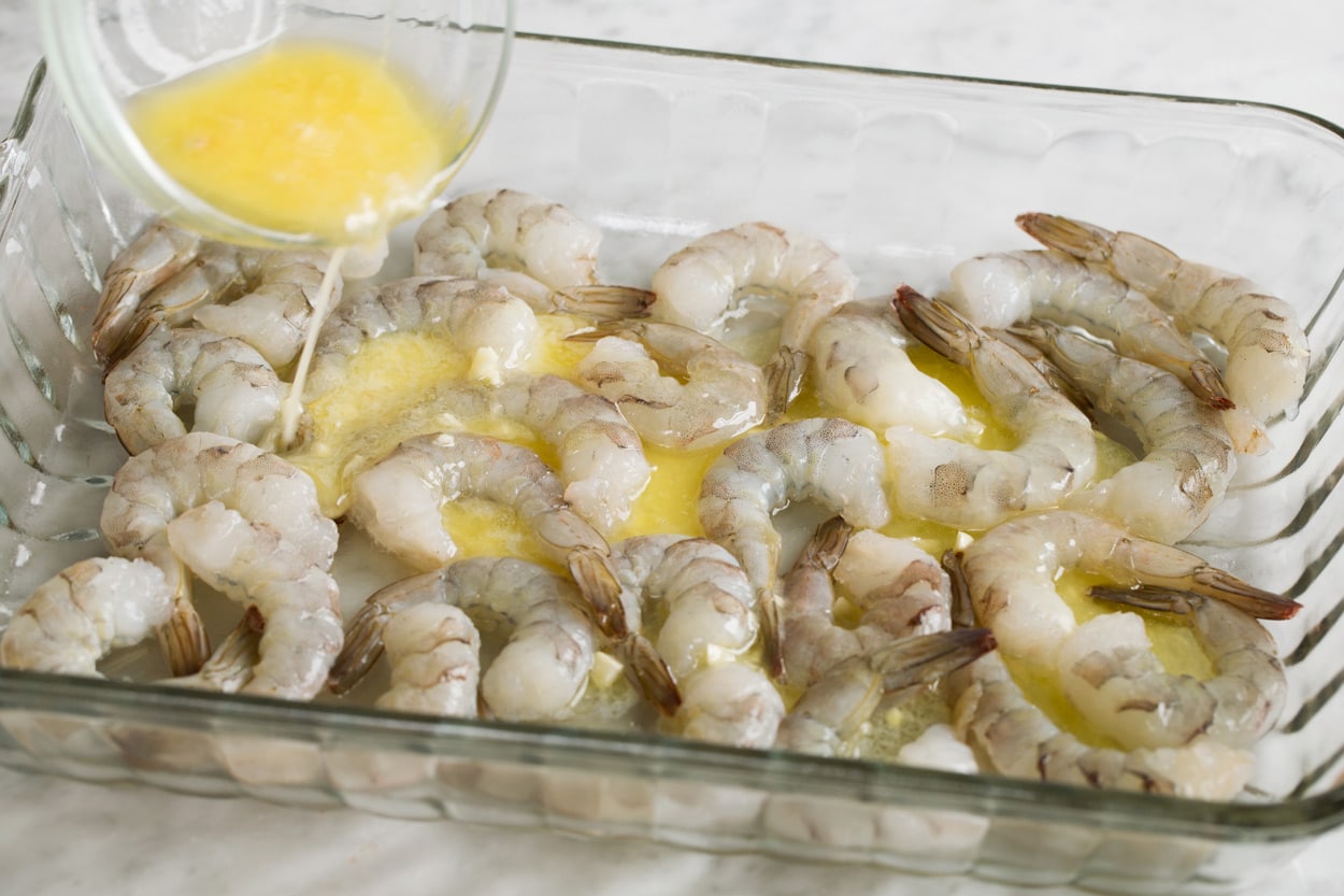 Showing how to make baked shrimp. Pouring garlic lemon butter over shrimp in baking dish. 