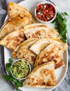 Overhead image of 8 quesadilla wedges on a white oblong platter served with pico and guacamole.