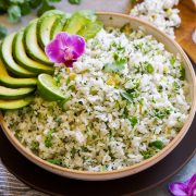 Serving bowl full of cilantro lime rice garnished with avocado slices, cilantro leaves, orchid flower and lime.