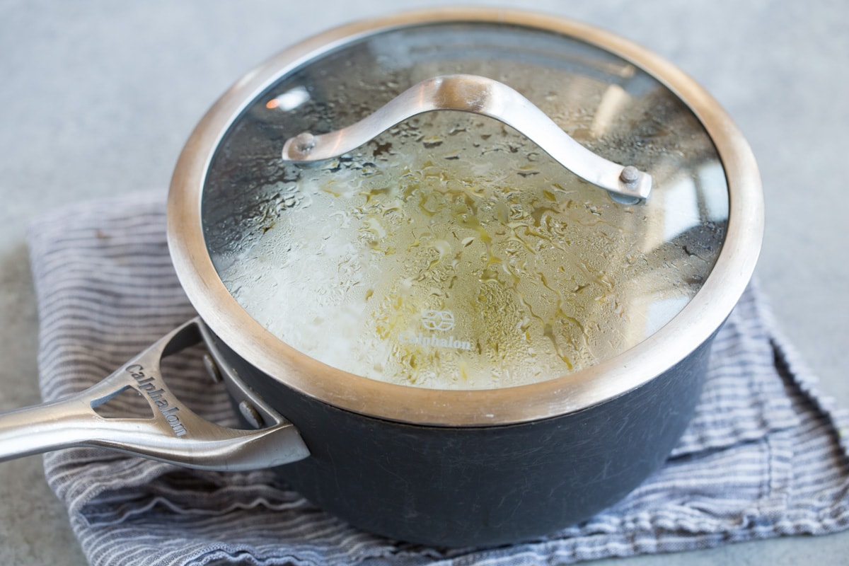 Resting cilantro lime rice in a saucepan covered with a lid off heat on a grey napkin.