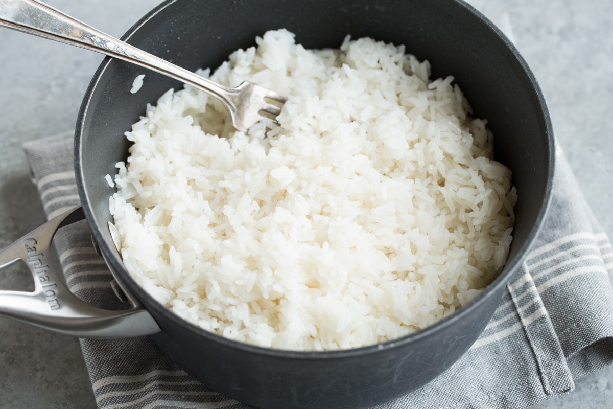 Fluffing finished coconut rice in saucepan with a fork.