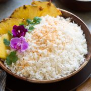 Coconut rice in a wooden bowl set over a brown plate on a grey surface.