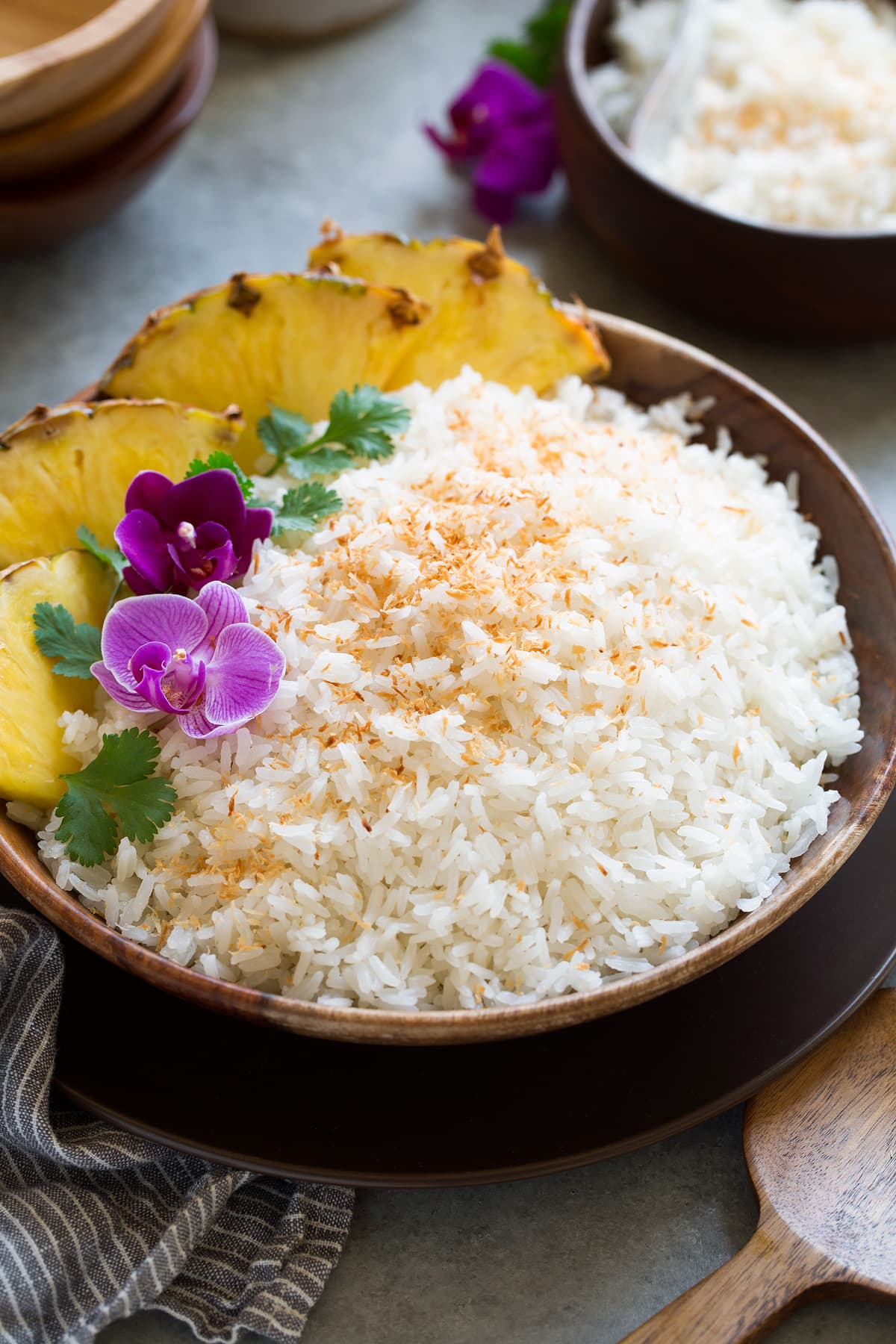 Coconut rice in a wooden bowl set over a brown plate on a grey surface.