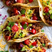 Row of ground beef tacos on parchment paper.