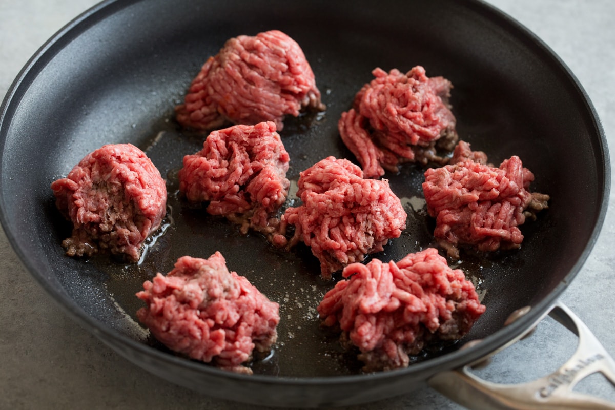 Showing how to make tacos. Searing ground beef in chunks in a non-stick skillet to brown.