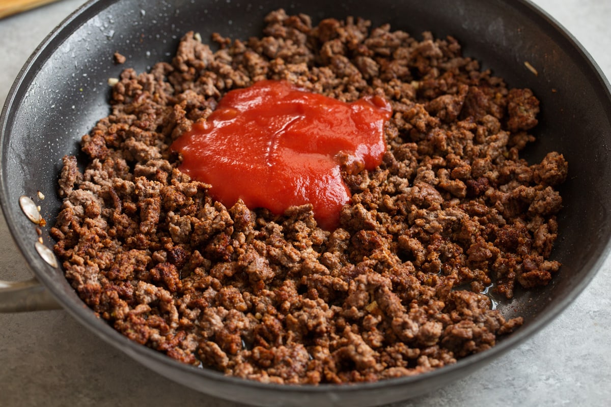 Adding tomato sauce and chicken broth to taco meat filling in skillet.