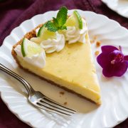 Slice of Best Key Lime Pie on white scalloped dessert plate set over a maroon napkin.