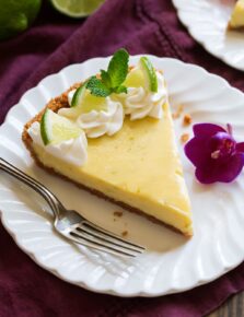 Slice of Best Key Lime Pie on white scalloped dessert plate set over a maroon napkin.