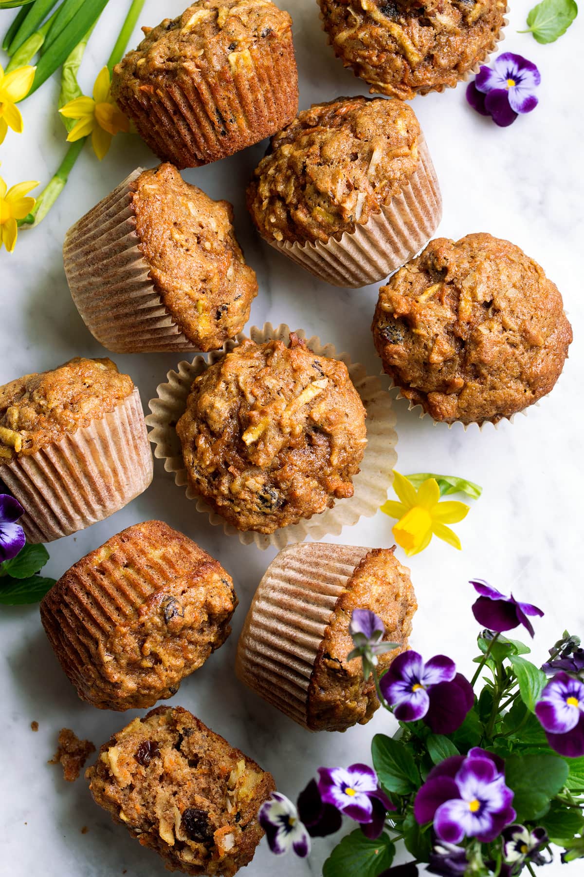 Overhead image of morning glory muffins on a marble surface decorated with spring flowers.