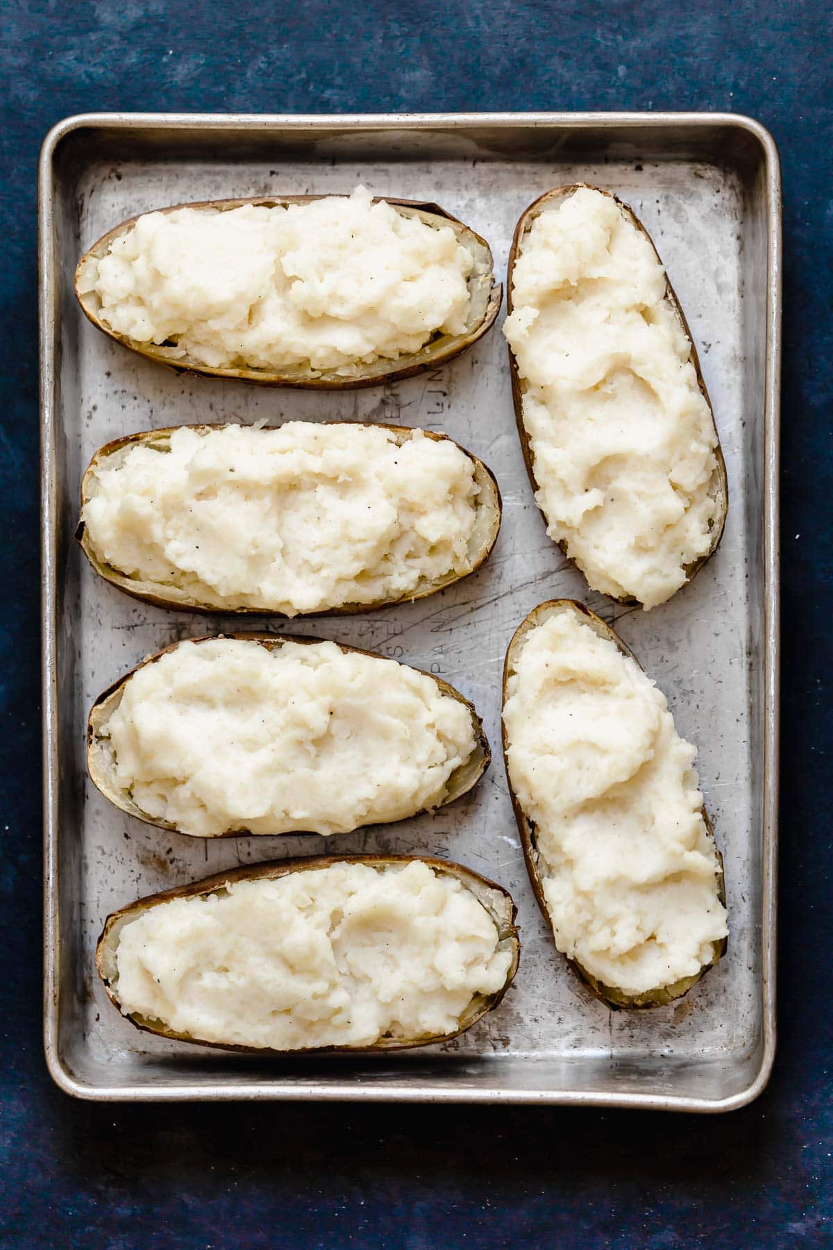 Six potato skins filled with mashed potatoes sitting on a metal baking dish.