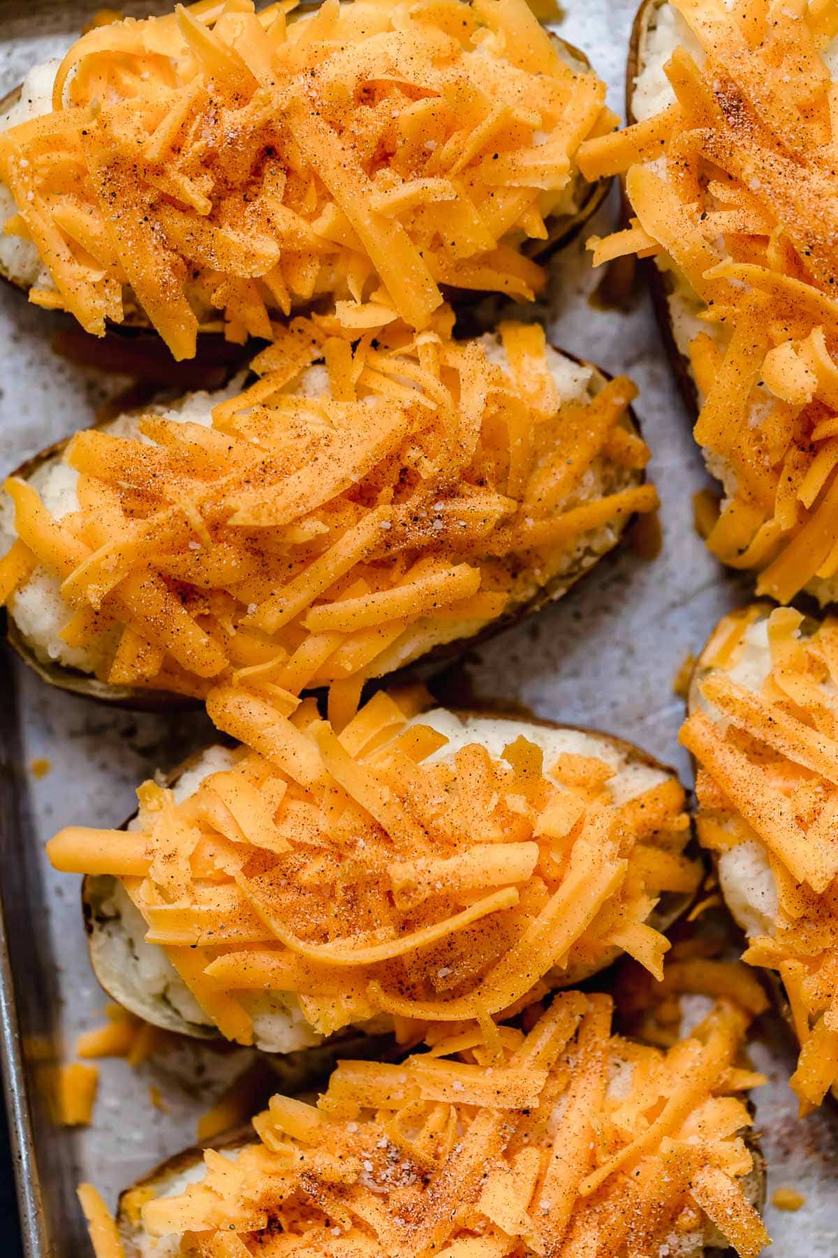 Twice baked potatoes filled with mashed potatoes and topped with shredded cheddar and seasoning. Shown before baking.