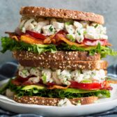 Stack of two chicken salad sandwiches on a white plate set over a dark grey cloth.