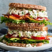 Stack of two chicken salad sandwiches on a white plate set over a dark grey cloth.