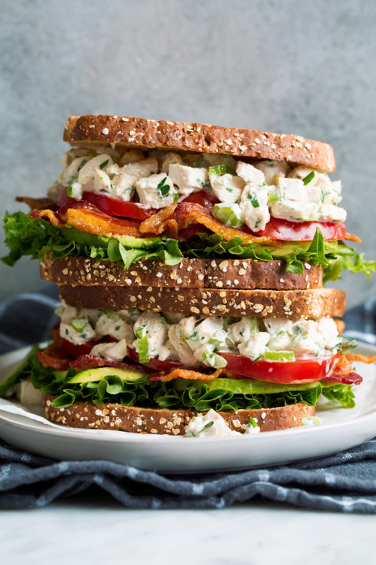 Stack of two chicken salad sandwiches on a white plate set over a dark grey cloth.