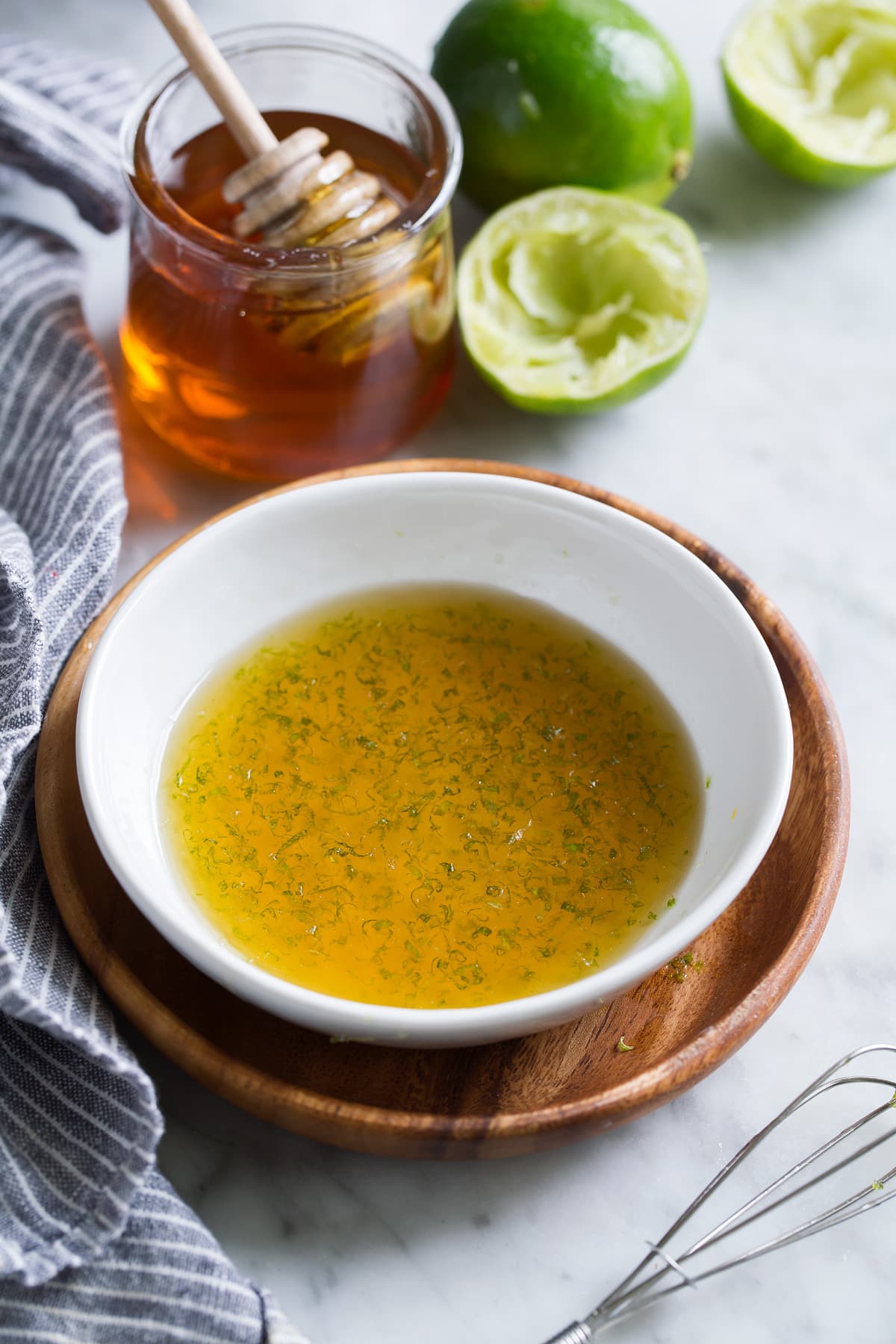 Honey lime fruit salad dressing in a small white bowl set over a wooden plate.