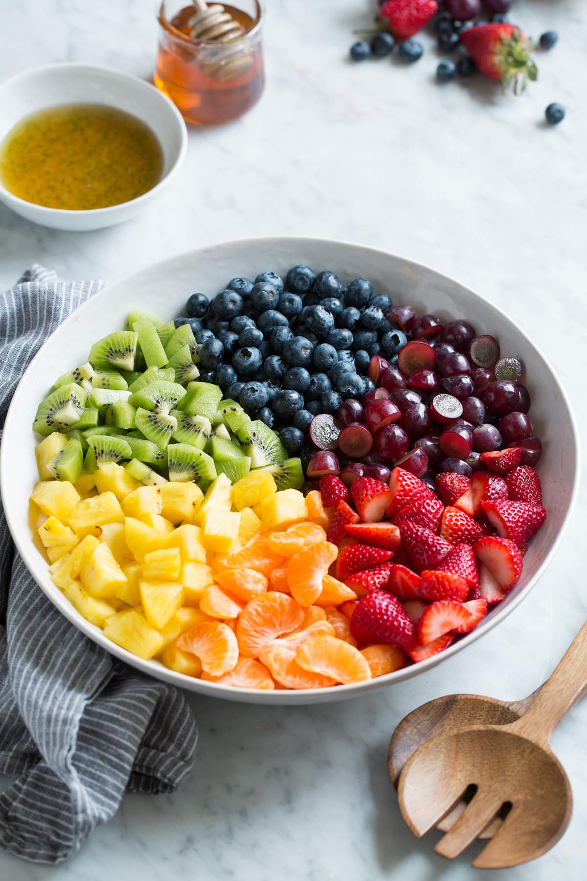 Fresh strawberries, mandarin oranges, pineapple, kiwi, blueberries, and grapes in sections in a large white serving bowl.