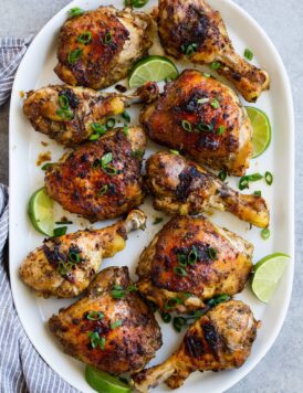 10 pieces of jerk chicken, combination of thighs and legs, on a white oval platter set over a grey surface.