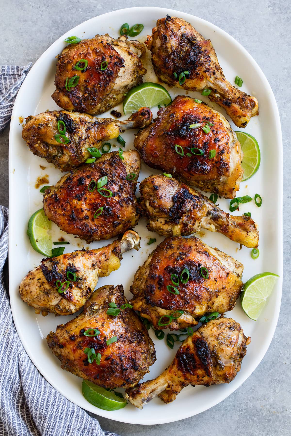 10 pieces of jerk chicken, combination of thighs and legs, on a white oval platter set over a grey surface.